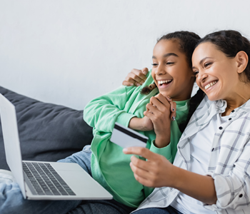 a mother and daughter holding a debit card with a laptop in front of them